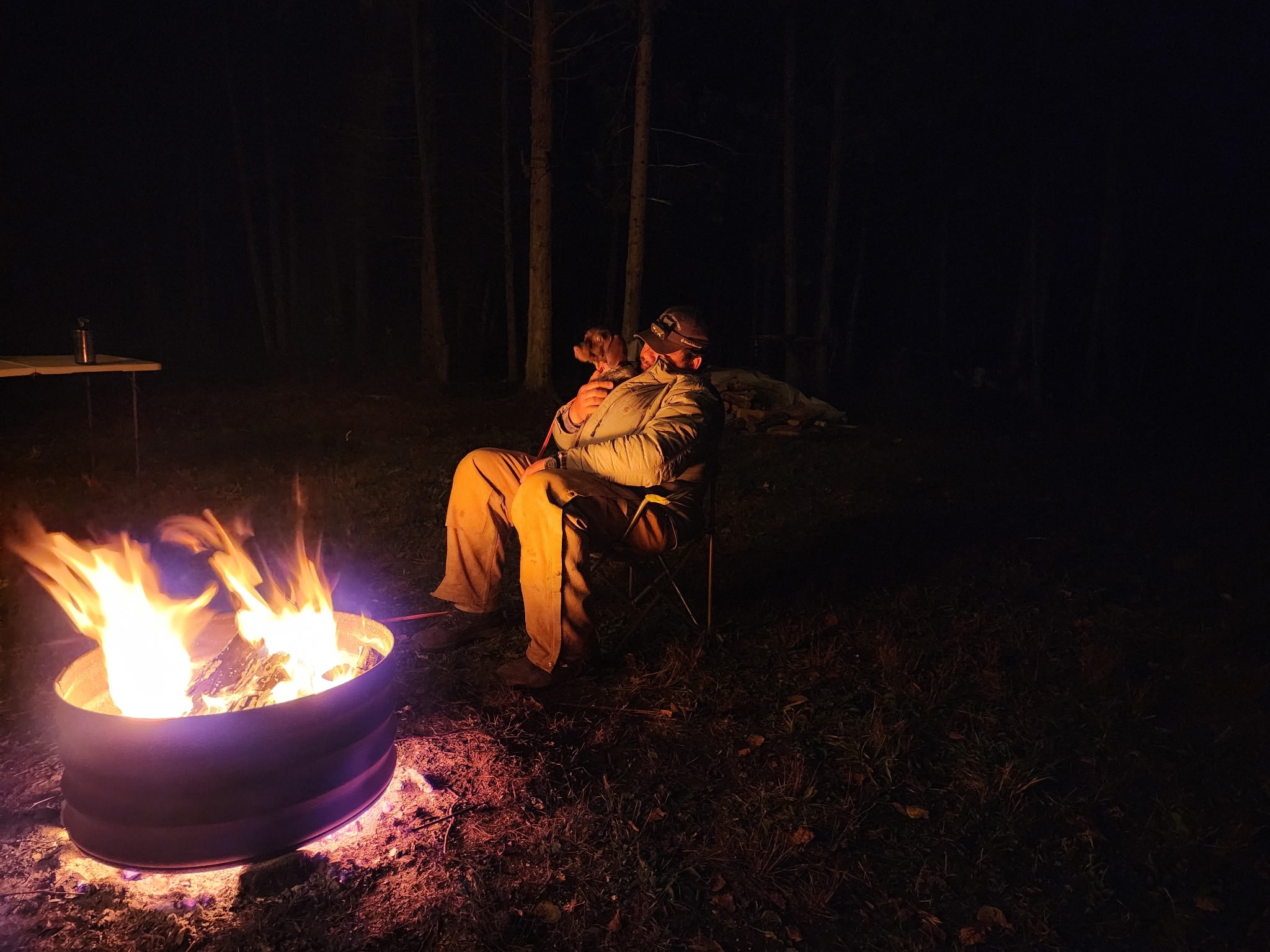 A hunter sits with his gundog beside a campfire at night in the Upper Peninsula woods.