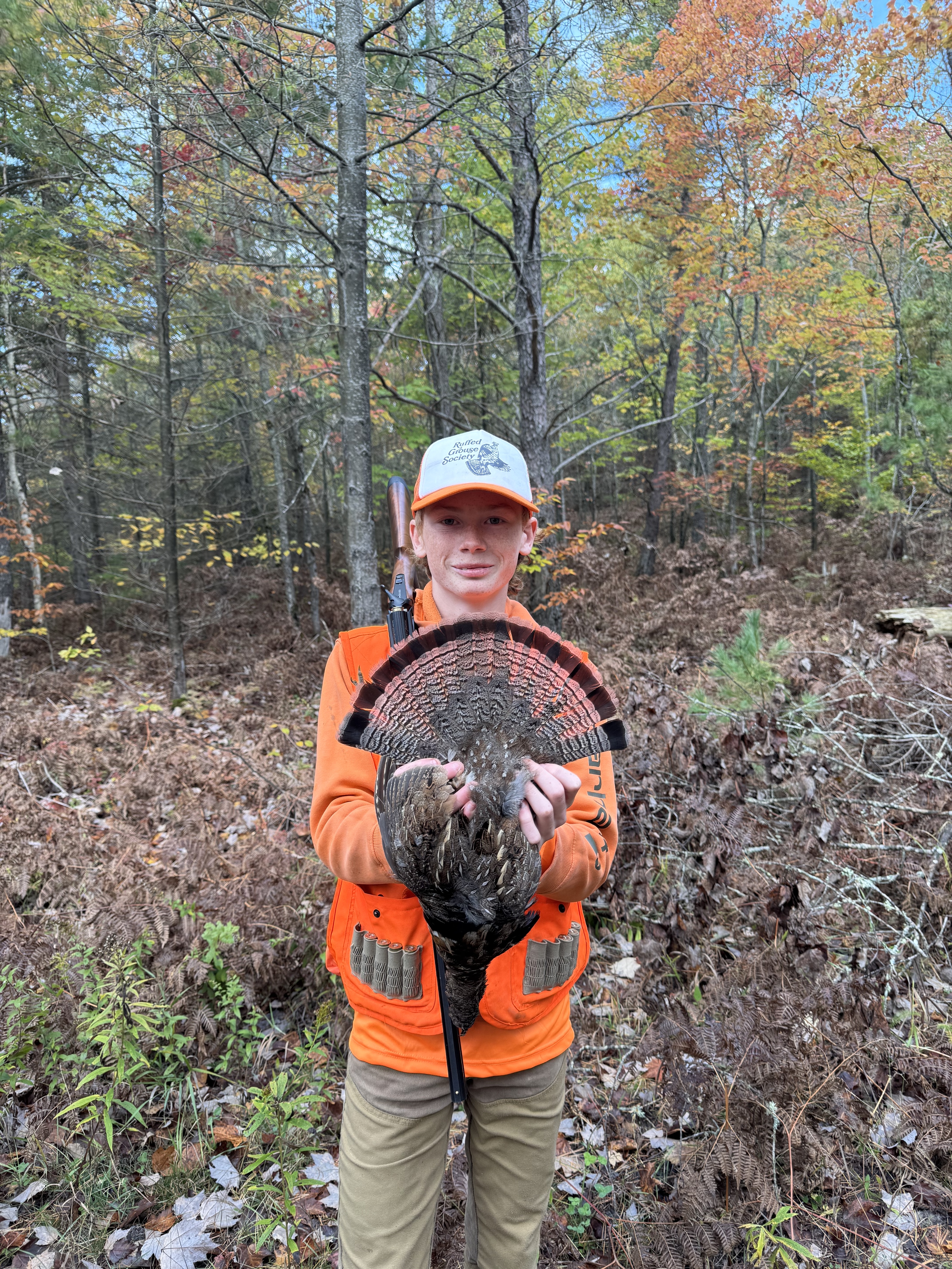 A young hunter holds up a fanned ruffed grouse tail beside a happy German Shorthaired Pointer.